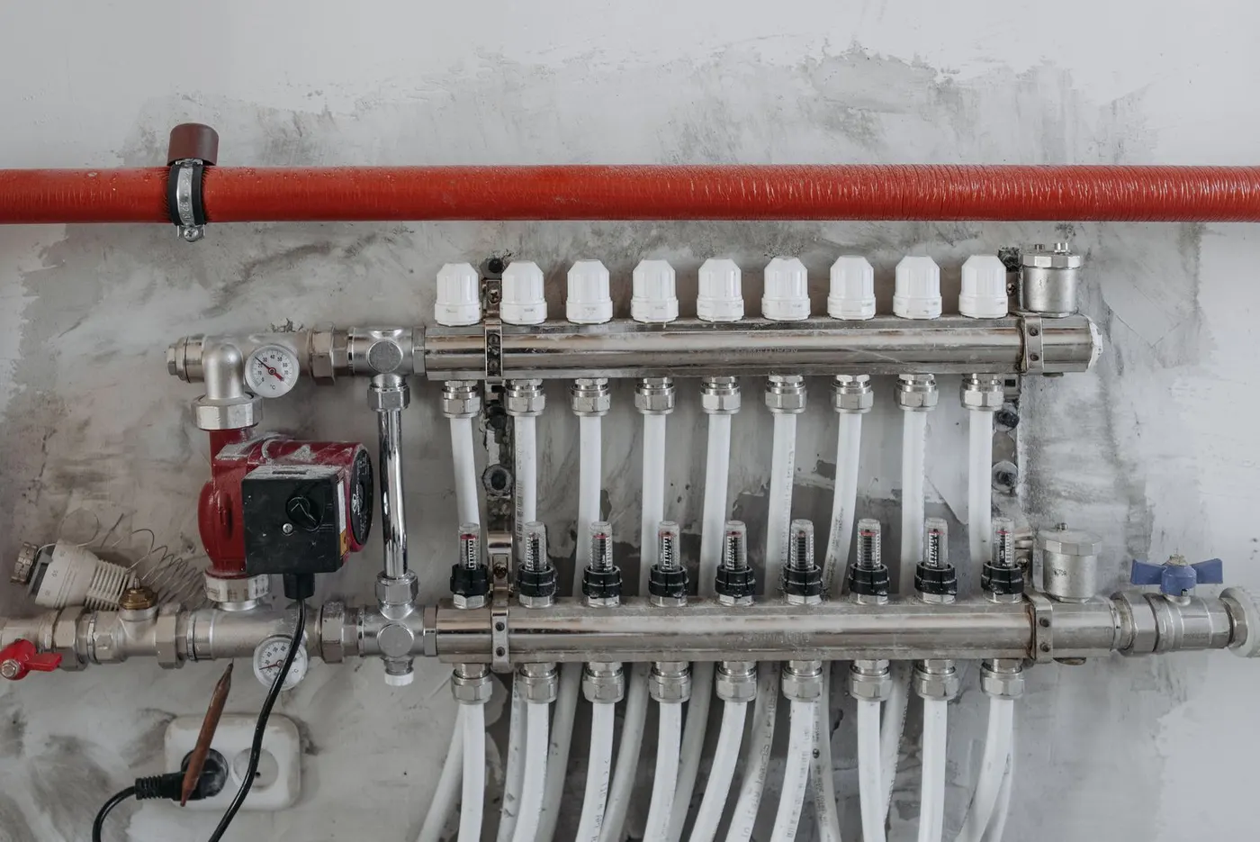 Heizkreisverteiler mit Umwälzpumpe, Manometern und Durchflussanzeigern an einer Kellerwand